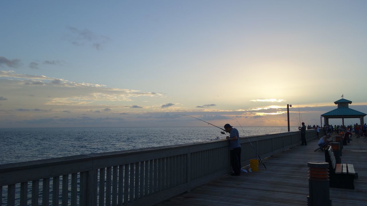 PEOPLE STANDING AT BEACH DURING SUNSET