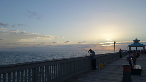 People standing on beach against sky during sunset