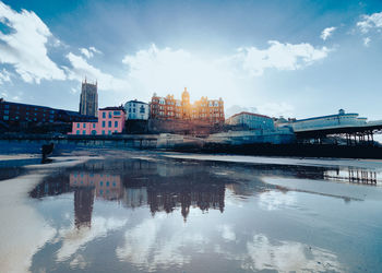 Buildings by river against sky in city