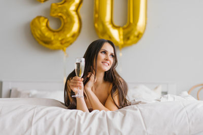 Beautiful woman woke up in bed in the morning and celebrates her thirties with a glass of champagne