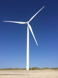Low angle view of windmill on landscape against blue sky