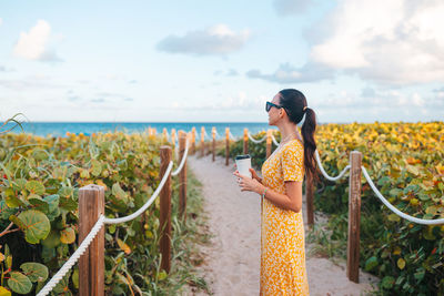 Rear view of woman standing by railing against sky