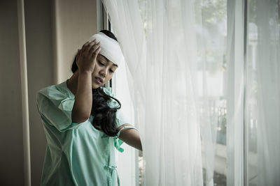 Woman with bandage on head standing by window at hospital