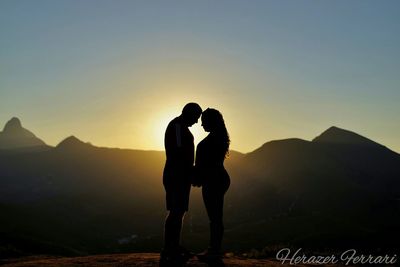 Silhouette couple standing on mountain against sky during sunset