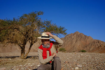 Senior man sitting at desert against clear blue sky