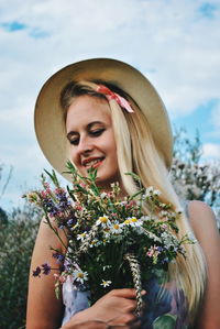 Young woman holding flowers against sky