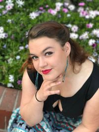 High angle portrait of young woman sitting on retaining wall against plants