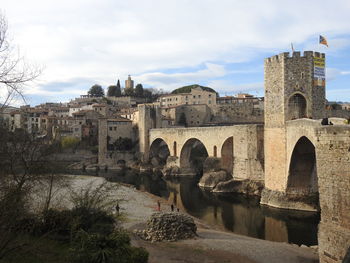 Arch bridge over river by buildings against sky