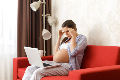 Young woman using mobile phone while sitting on sofa at home