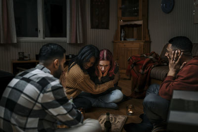 Terrified multiracial friends with ouija board in haunted cabin