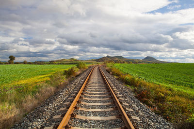 View of railroad tracks on field against cloudy sky