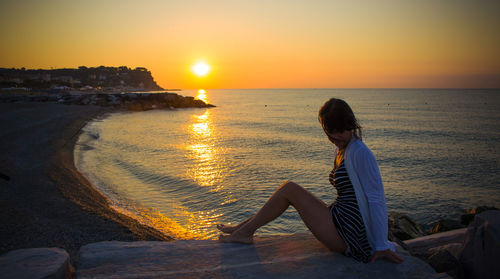 Rear view of woman sitting on beach during sunset