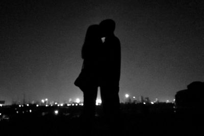 Silhouette of man with arms outstretched against sky at night