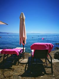 Chairs and table at beach against clear blue sky