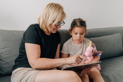 Grandmother teaching granddaughter through digital tablet at home