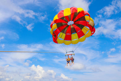 Low angle view of people parasailing against sky