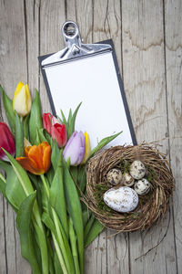 High angle view of colorful eggs and flowers with note pad on table