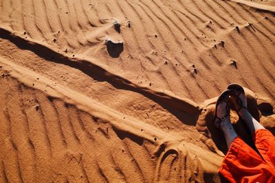 Low section of woman sitting on sand at desert