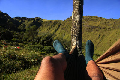 Low section of man lying on hammock against green mountain
