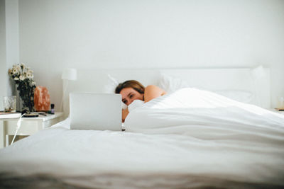 Woman using laptop while lying on bed at home