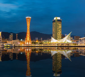 Illuminated buildings by lake against sky at night