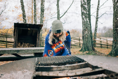 Woman sat by a campfire wrapped in a blanket in the forest in sweden