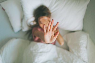 Directly above shot of woman showing stop sign while sleeping on bed at home