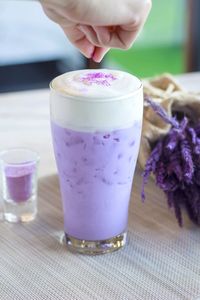 Cropped hand sprinkling ingredient in purple drink on table