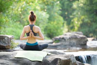 Rear view of woman standing on rock against trees