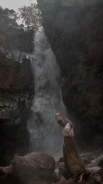 Full length of woman standing on rock against waterfall