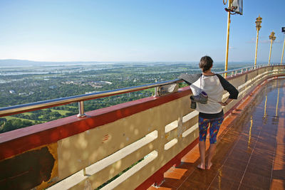Rear view of man standing on railing against sky