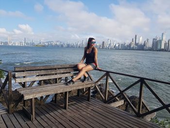 Woman sitting on bridge against sky