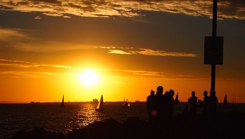 Silhouette people by sea against sky during sunset