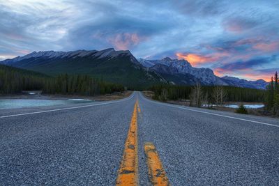 Highway and mountains against cloudy sky during sunset