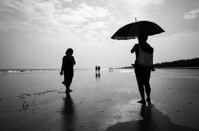 Silhouette people standing on beach against sky