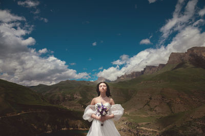 Young woman standing on mountain against sky