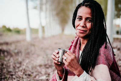 Portrait of smiling woman holding coffee cup sitting at park