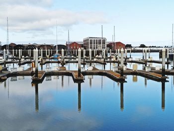 Sailboats moored in harbor by buildings against sky