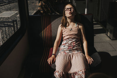 Girl with eyes closed making face while traveling in train
