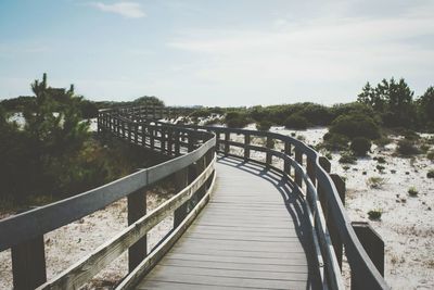 Wooden bridge on beach against cloudy sky