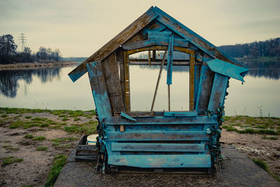 Lifeguard hut on field by lake against sky