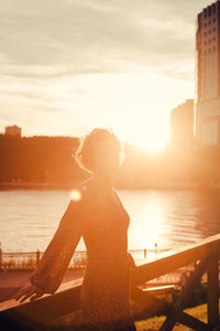 Rear view of woman sitting against sky during sunset