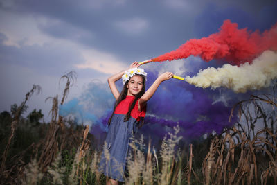 Portrait of smiling cute girl holding distress flares while standing against sky at dusk