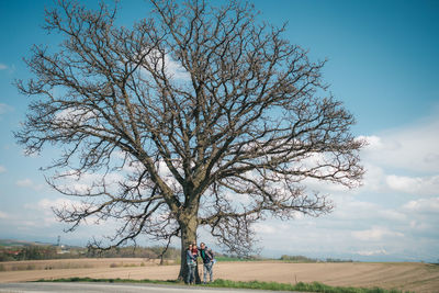 Woman standing by tree on field against sky