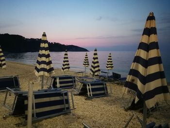 Deck chairs on beach against sky during sunset