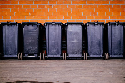 Garbage can in a row in front of brick wall