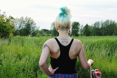 Rear view of woman with skateboard on grassy field