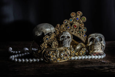 Close-up of human skulls and gold jewelry on table against black background