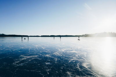 People ice-skating on frozen lake against sky on sunny day