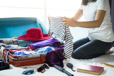 Low section of woman packing luggage on bed at home